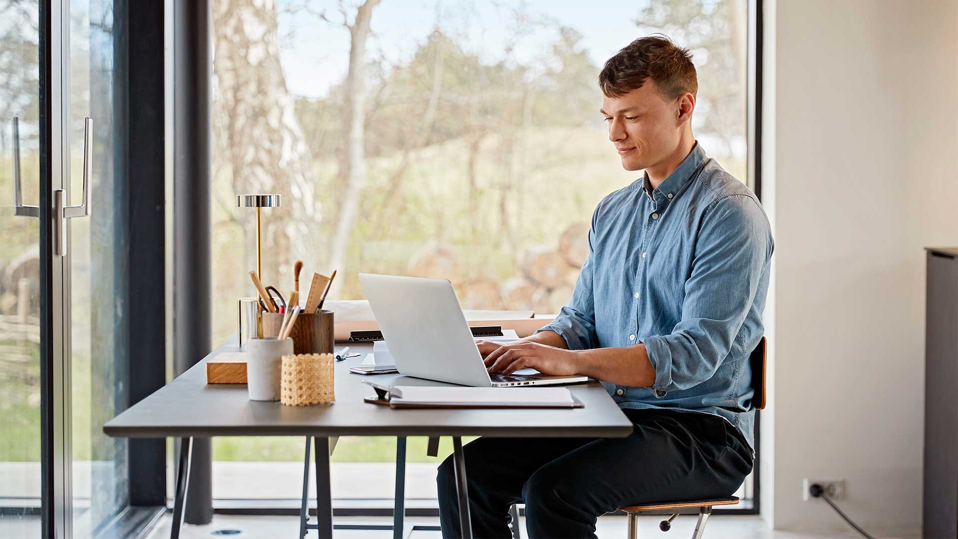 Ung mad sidder med pc på sin hjemmearbejdsplads. Han arbejder effektiv med fiberbredbånd. Han har fået gode råd til, hvordan han arbejder bedst hjemmefra.