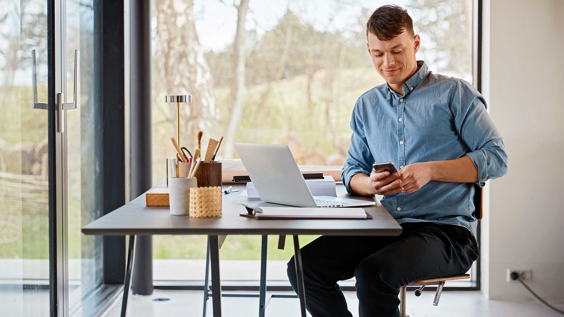 Mand sidder ved skrivebord med pc og mobil.  Han undersøger hvilken trådløs router er den bedste router til fibernet.