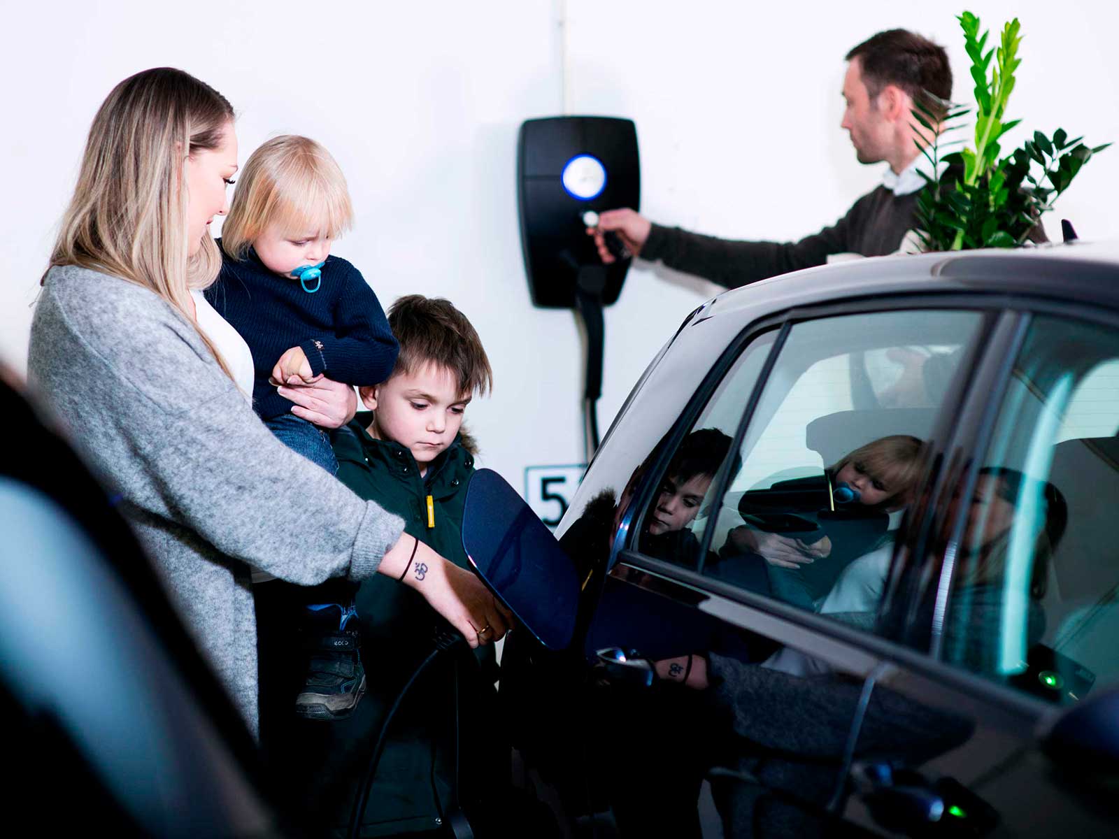 Familie ved elbil og ladeboks, der oplader deres elbil