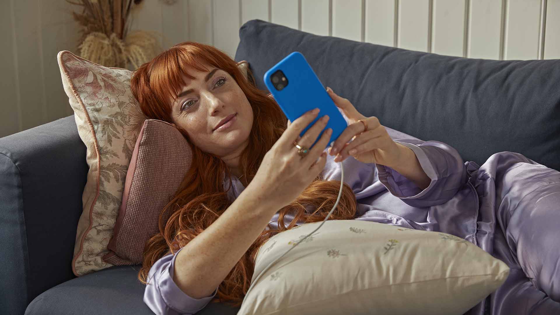 Kvinde ligger i sofa med mobil. Hun skal vælge det bedste internet, men hvad er forskellen på bredbånd og fibernet? Vi undersøger det her.