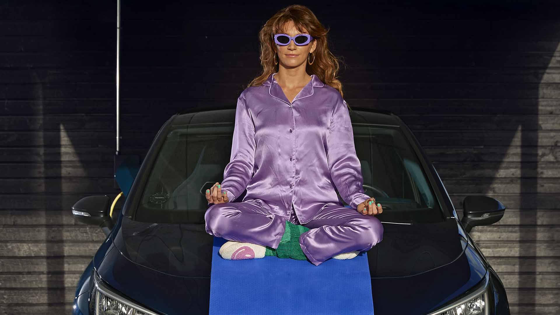 Kvinde sidder på yogamåtte på køleren af sin elbil