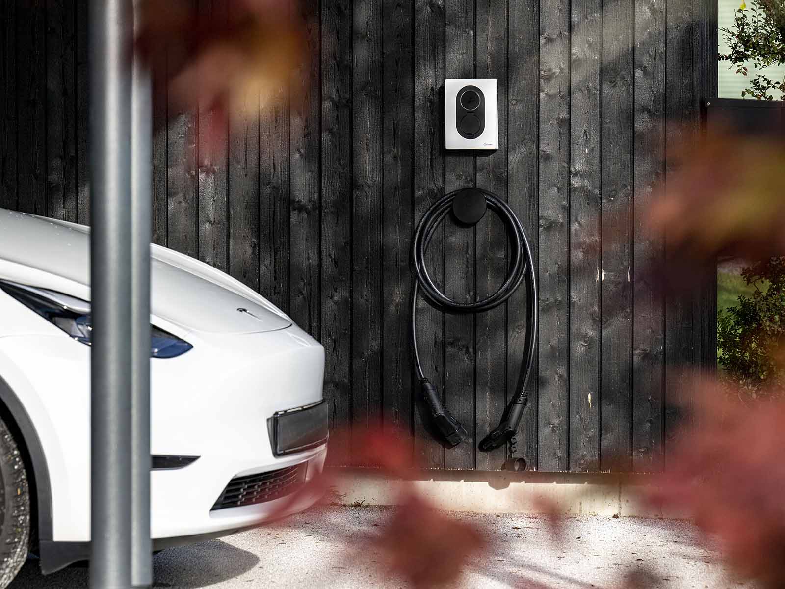 Tesla i carport med ladeboks ved sommerhus. Oplad din elbil nemt og nyd ferien med en ladestander til sommerhuset fra EWII.