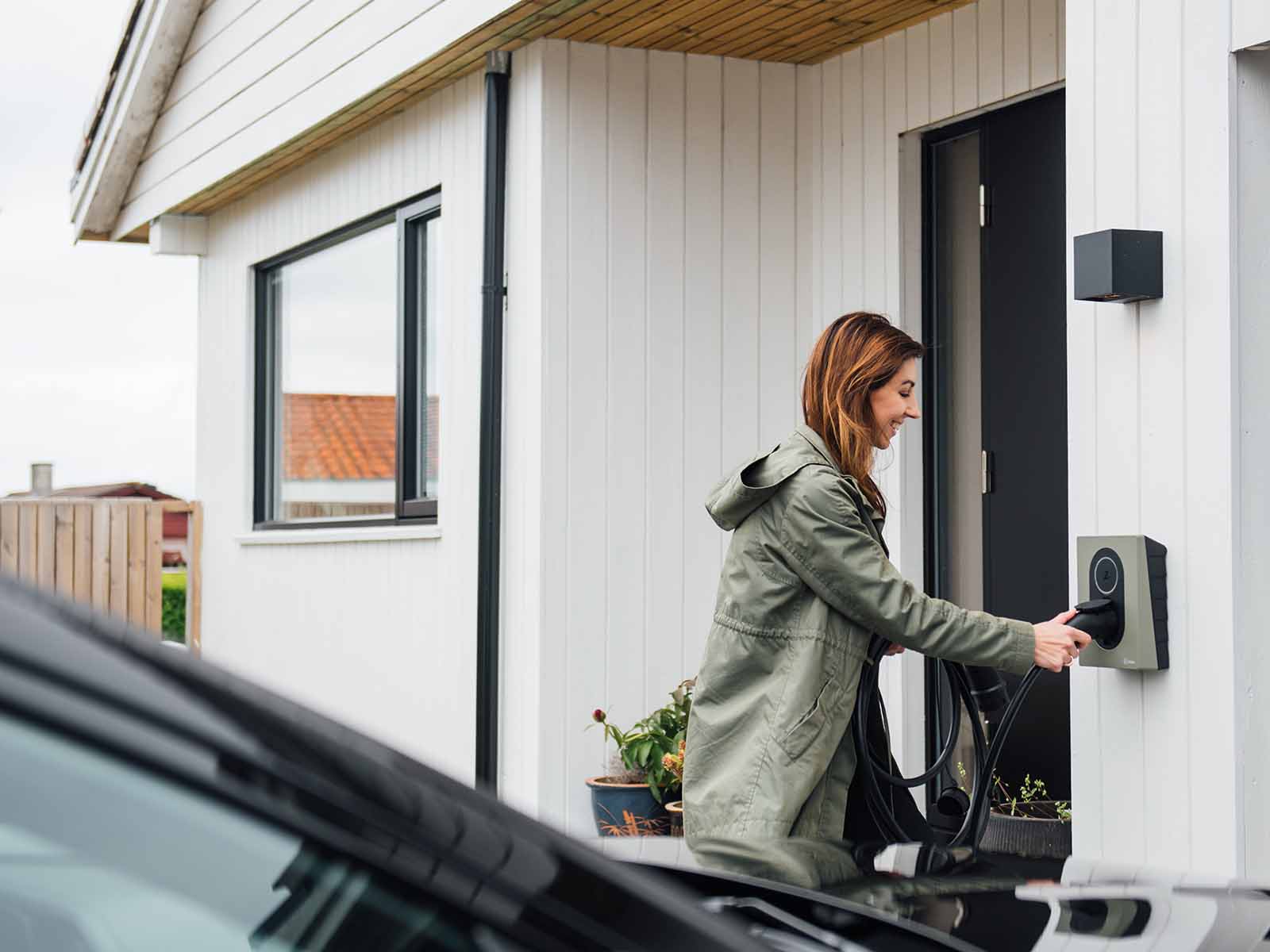 Kvinde sætter elbil til at lade ved sommerhus. Med en ladestander til sommerhuset gør du det nemt for dine lejere at nyde ferien.